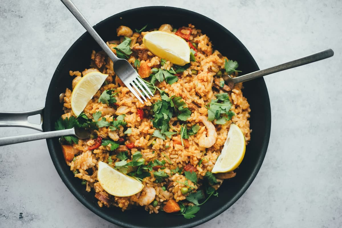 Pan of seafood rice with lemon wedges and herbs